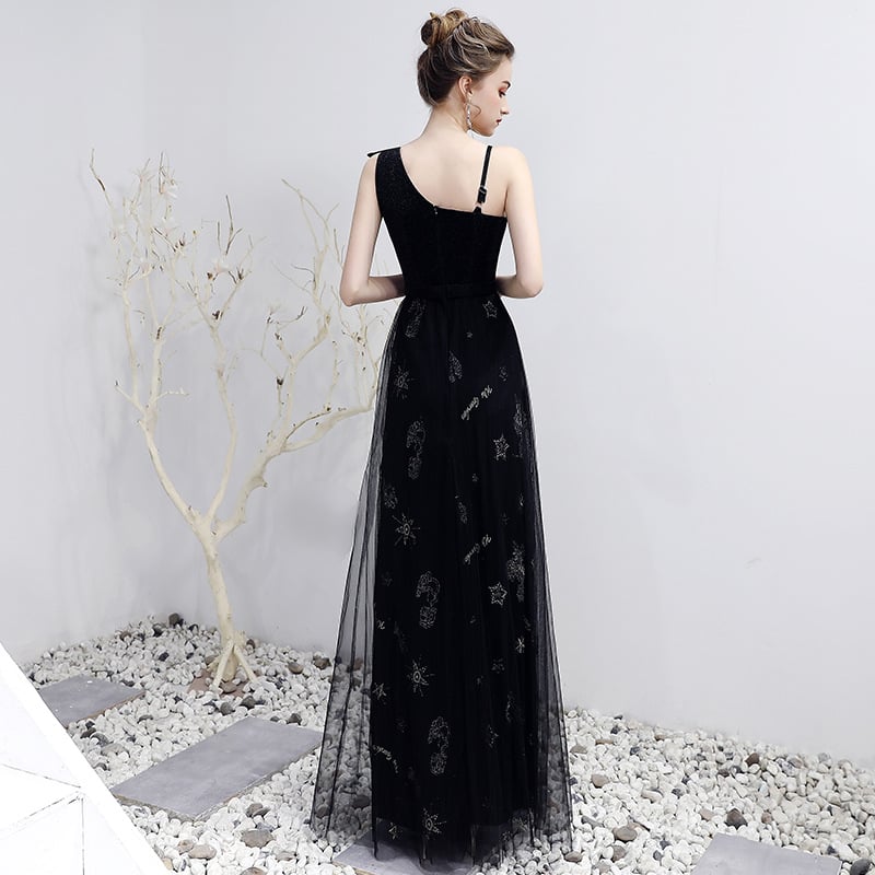 Frau in elegantem, schwarzem Abendkleid mit Sternenmuster, steht vor weißer Wand und dekorativem, kahlem Baum. Elegante Mode, Abendgarderobe.