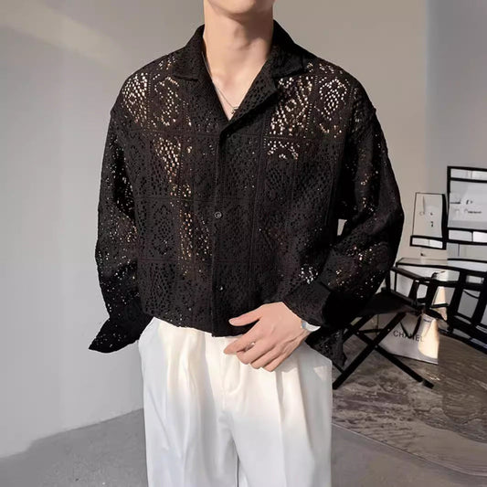 Ein Mann trägt ein schwarzes, durchbrochenes Hemd mit geometrischem Muster und weiße Hosen. Moderner, eleganter Herrenstil, modische Kleidung.