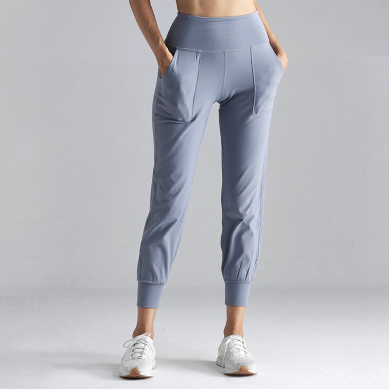 Damen-Sporthose in Hellblau, hohe Taille, seitliche Taschen, elastische Bündchen, kombiniert mit weißen Sneakers, ideal für Fitness und Freizeit.