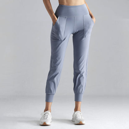 Damen-Sporthose in Hellblau, hohe Taille, seitliche Taschen, elastische Bündchen, kombiniert mit weißen Sneakers, ideal für Fitness und Freizeit.