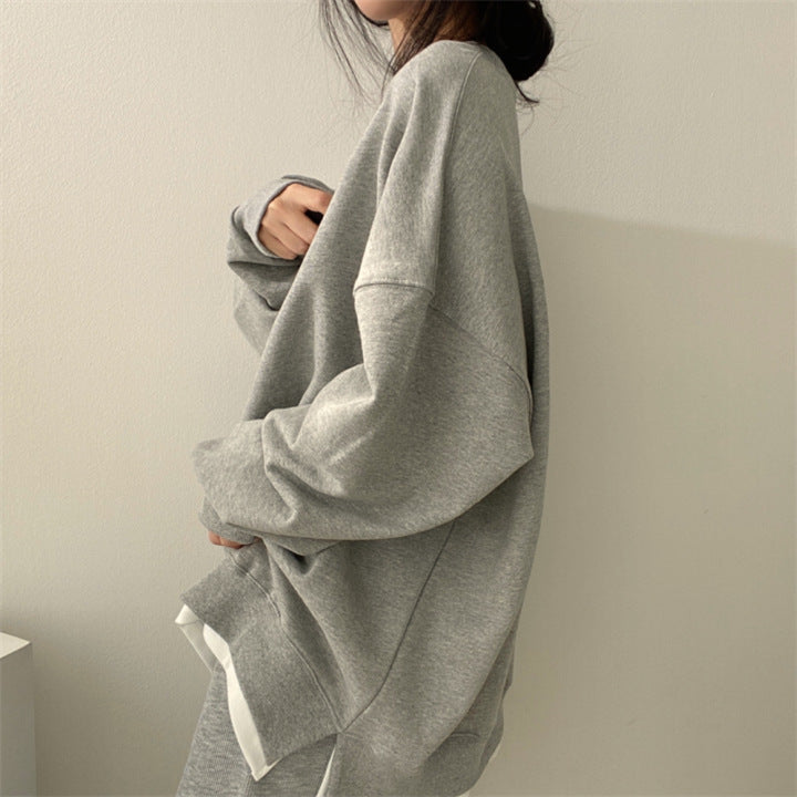 Grauer Oversize-Pullover, lässig getragen von einer Person, minimalistische Mode, gemütlicher Look, weicher Stoff, trendige Freizeitkleidung.