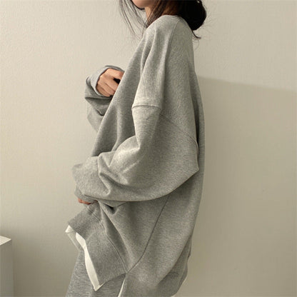 Grauer Oversize-Pullover, lässig getragen von einer Person, minimalistische Mode, gemütlicher Look, weicher Stoff, trendige Freizeitkleidung.