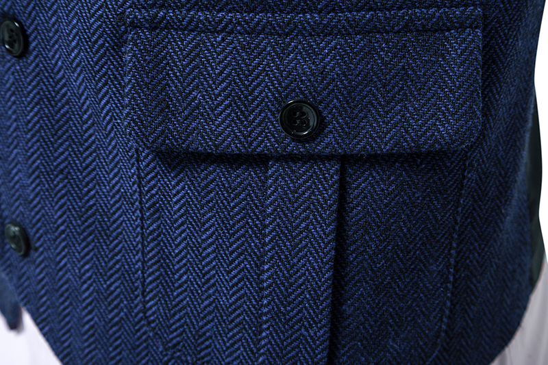 Nahaufnahme einer blauen Fischgrät-Jacke mit schwarzen Knöpfen und einer Tasche. Hochwertige Herrenmode, elegantes Design, stilvolle Textur.