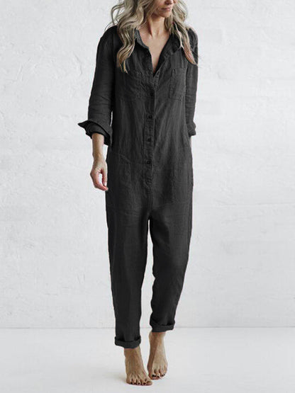 Frau in schwarzem Leinen-Jumpsuit, barfuß, vor weißer Wand. Modetrend, lässiger Einteiler, minimalistischer Stil, bequemes Outfit.