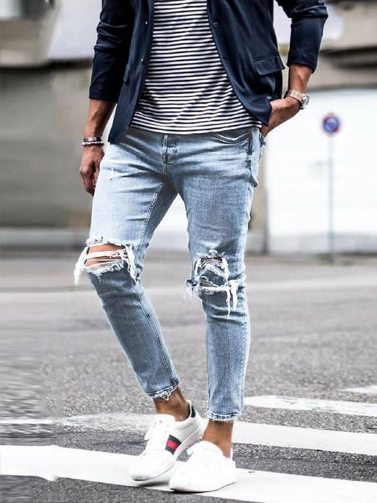 Mann in zerrissener Jeans, gestreiftem T-Shirt und Blazer auf Straße. Modetrend, lässiger Stil, urbane Herrenmode, weiße Sneaker.