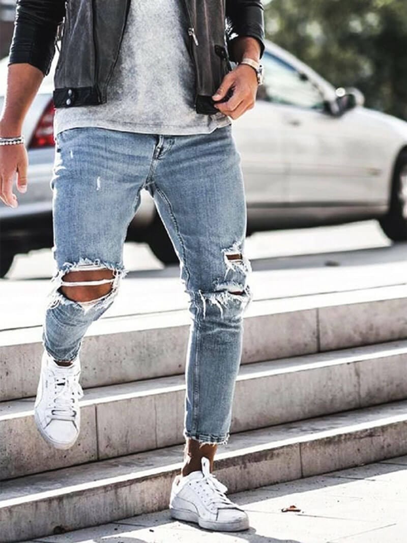 Mann in zerrissenen Jeans und Lederjacke geht Treppe hinunter, weiße Sneaker, urbaner Stil, modische Herrenbekleidung, Straßenmode.