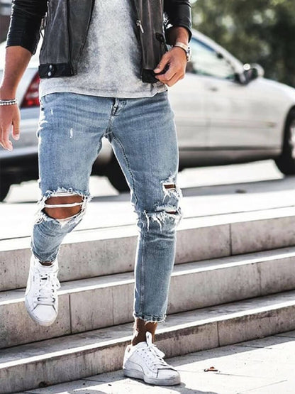 Mann in zerrissenen Jeans und Lederjacke geht Treppe hinunter, weiße Sneaker, urbaner Stil, modische Herrenbekleidung, Straßenmode.