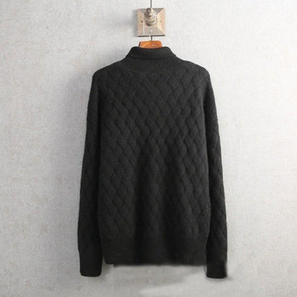 Schwarzer Strickpullover mit Zopfmuster, hängend an Holzbügel vor grauer Wand. Modischer Herrenpullover, warm und stilvoll für Herbst und Winter.