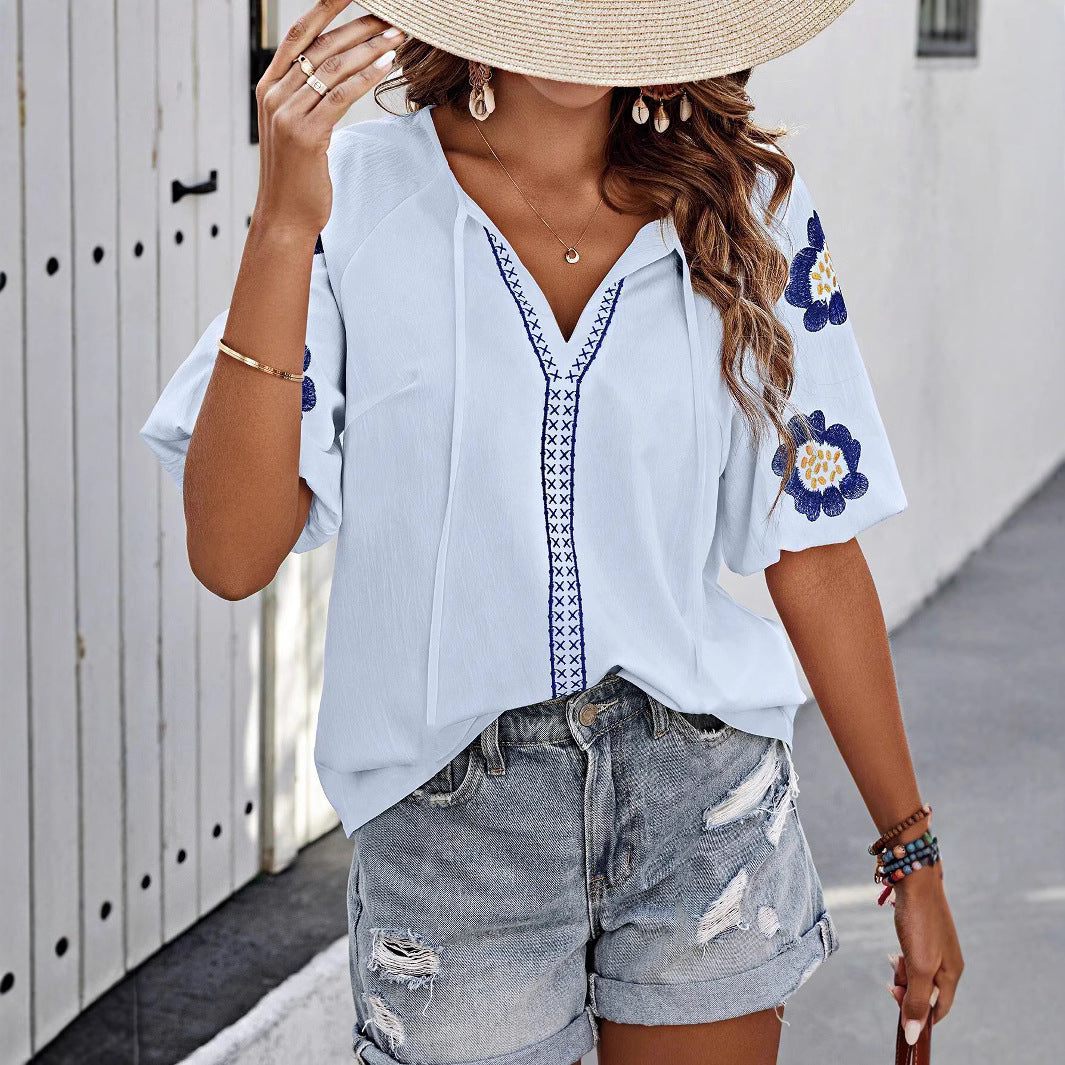 Frau in blauer bestickter Bluse und zerrissenen Jeansshorts, trägt Strohhut, steht vor weißer Wand. Sommermode, lässiger Stil, Boho-Chic.