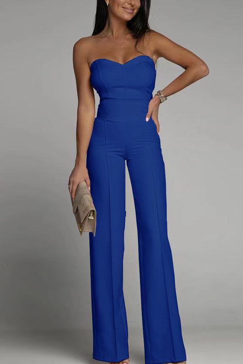 Frau in blauem, schulterfreiem Jumpsuit, hält eine beige Clutch. Elegante Abendmode, modischer Look, stilvolle Damenbekleidung.