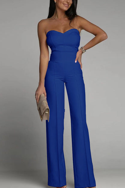 Frau in blauem, schulterfreiem Jumpsuit, hält eine beige Clutch. Elegante Abendmode, modischer Look, stilvolle Damenbekleidung.