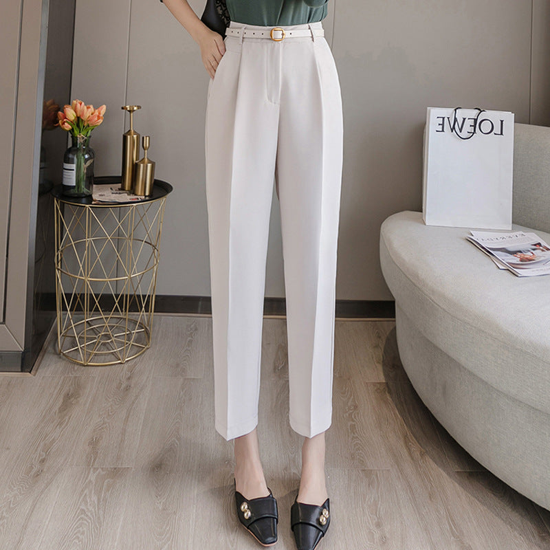 Damenhose in Weiß, elegant und modern, kombiniert mit schwarzen Loafers. Stilvolle Einrichtung im Hintergrund mit Blumen und Zeitschriften.