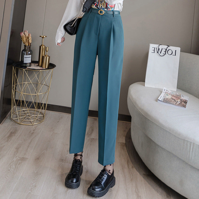 Elegante Damenhose in Türkis, kombiniert mit schwarzen Schnürschuhen. Moderne Wohnzimmerkulisse mit goldfarbenem Beistelltisch und Deko.