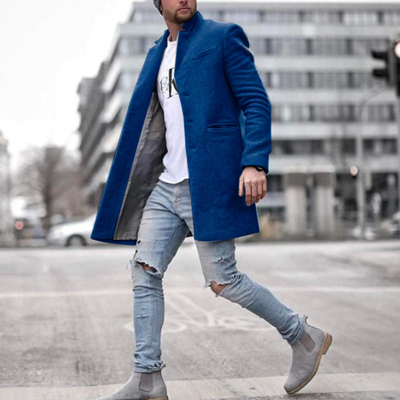 Mann in blauem Mantel und zerrissenen Jeans überquert Straße in urbaner Umgebung. Modetrend, Herrenmode, stilvoller Look.