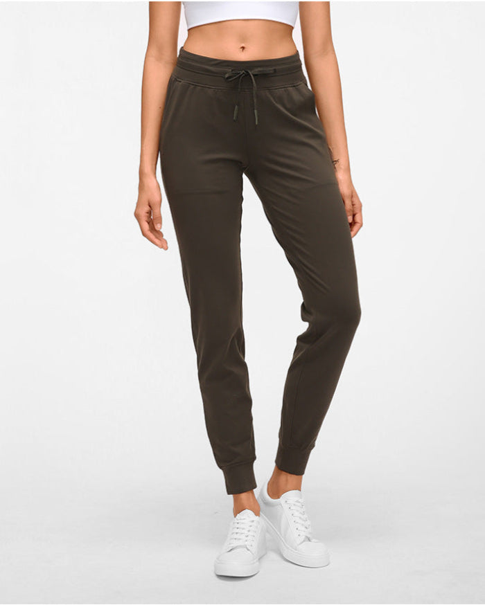 Frau in brauner Jogginghose und weißem Crop-Top, trägt weiße Sneaker. Sportliche Damenmode, bequeme Freizeitkleidung, modische Jogginghose.