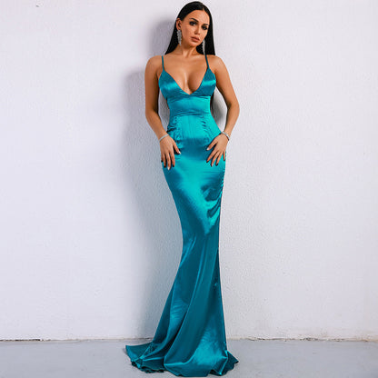 Frau in elegantem, türkisfarbenem Abendkleid mit tiefem Ausschnitt, posiert vor weißer Wand. Glamouröse Mode, Abendgarderobe, Satin-Kleid.