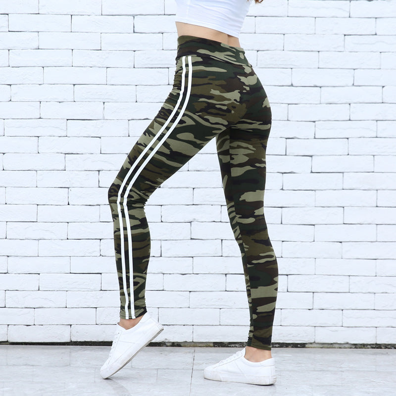 Damen-Camouflage-Leggings mit weißen Streifen, sportlich, modisch, vor weißer Ziegelwand, ideal für Fitness und Freizeit, kombiniert mit weißen Sneakers.