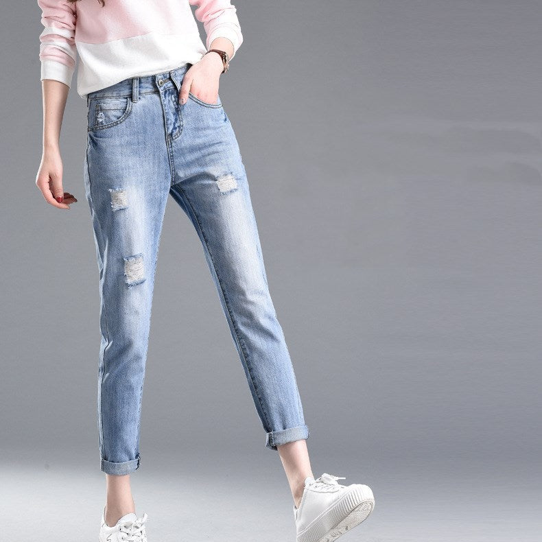 Damenjeans mit Rissen, lässiger Stil, kombiniert mit weißem Pullover und Sneakers. Modetrend, Freizeitlook, bequeme Passform.