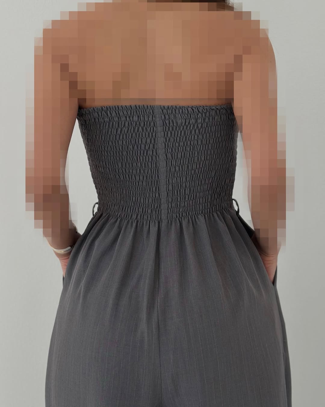 Rückenansicht einer Frau in einem schulterfreien, grauen, gerafften Kleid. Elegante Mode, Sommerkleid, schulterfreies Design.