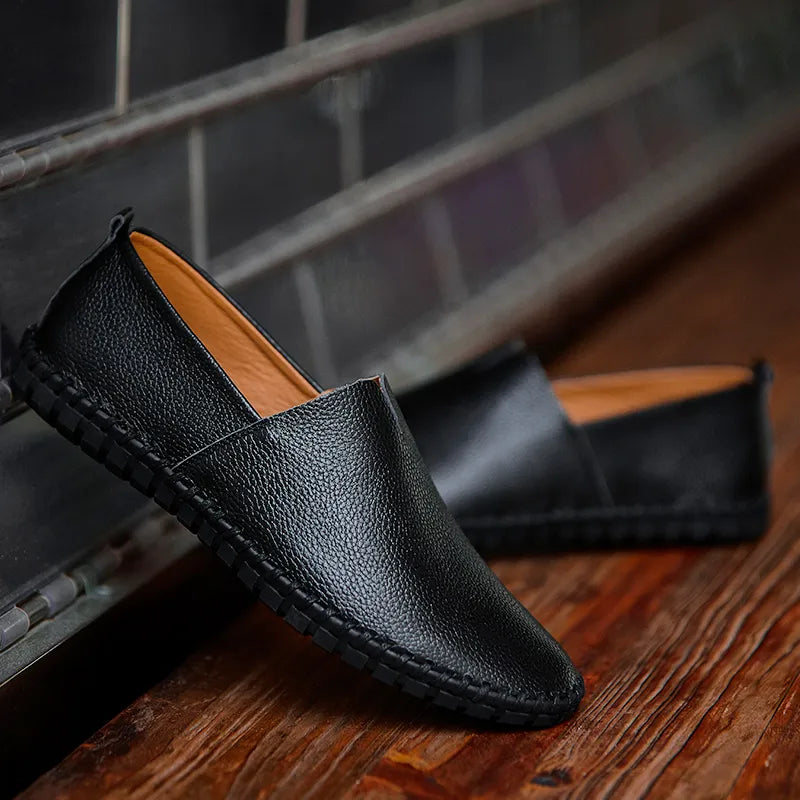 Schwarze Herren-Lederloafer auf Holzboden, seitlich angelehnt. Elegante, rutschfeste Freizeitschuhe, ideal für stilvolle Alltagsoutfits.