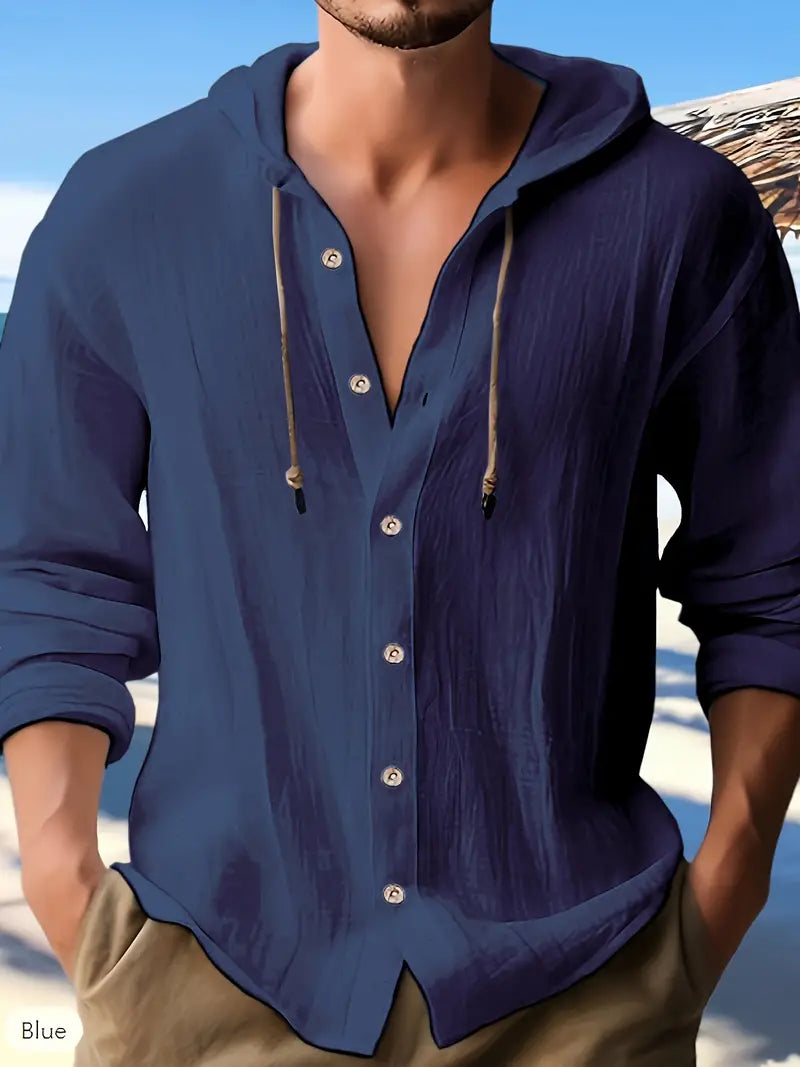 Mann in dunkelblauem Leinenhemd mit Kapuze am Strand, lässiger Sommerlook, modische Herrenbekleidung, entspannte Urlaubsatmosphäre.