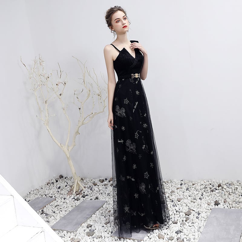Frau in elegantem, schwarzem Abendkleid mit Sternenmuster, posiert vor weißer Wand und dekorativem Baum. Mode, Abendgarderobe, Damenkleidung.