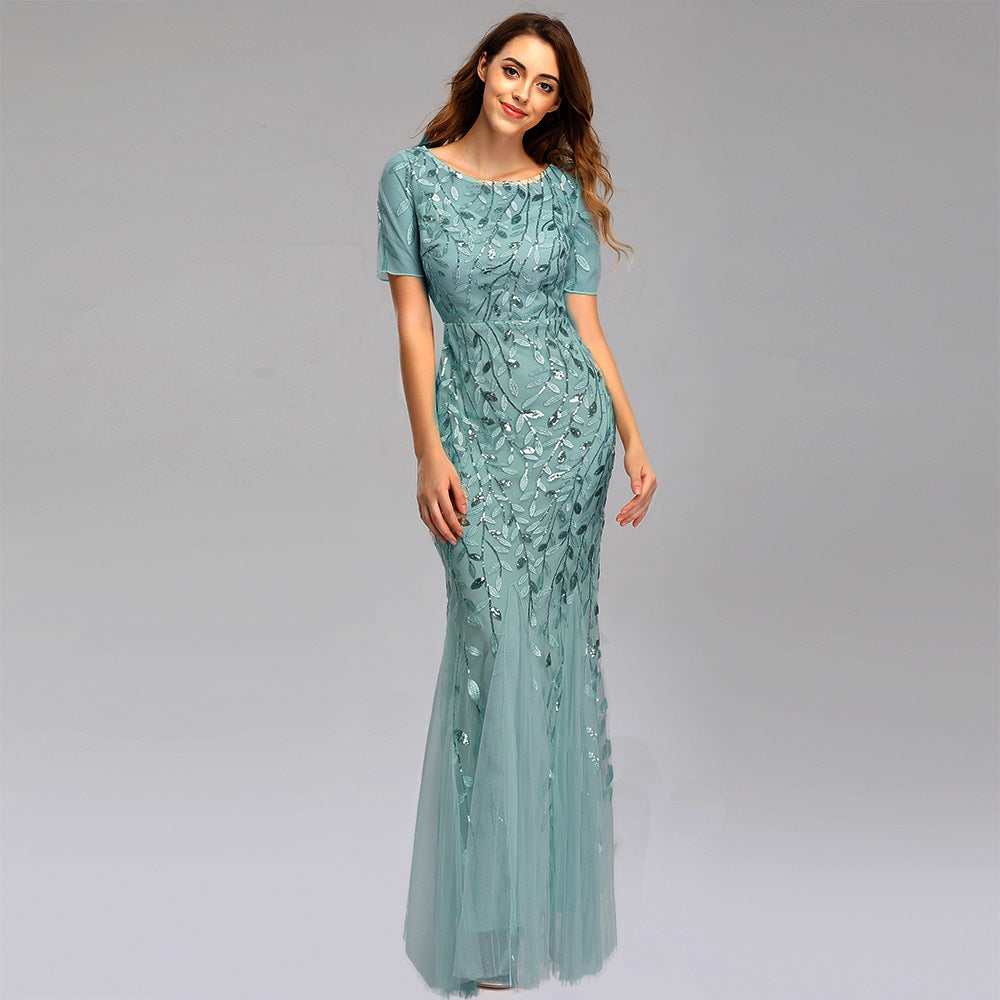 Frau in elegantem, langem, hellblauem Abendkleid mit floralen Stickereien, lächelt vor grauem Hintergrund. Perfekt für Gala oder Hochzeit.