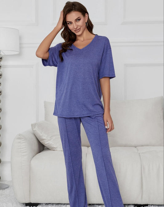 Frau in lila Pyjama-Set steht vor weißem Sofa in modernem Wohnzimmer. Bequeme Nachtwäsche, entspannte Atmosphäre, stilvolle Inneneinrichtung.