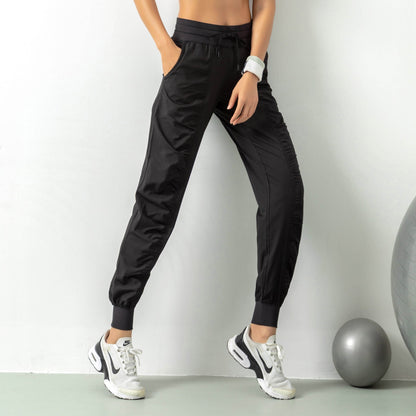 Frau in schwarzer Jogginghose und weißen Sneakers, steht neben einem grauen Gymnastikball. Sportliche Kleidung, Fitness, Freizeitmode.