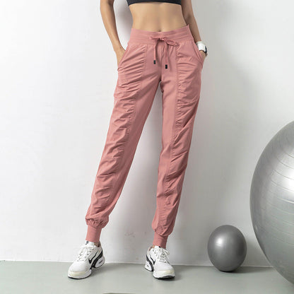 Frau in rosa Jogginghose und Sneakers steht neben Gymnastikball. Sportliche Kleidung, Fitnessmode, bequeme Jogginghose, Trainingsoutfit.