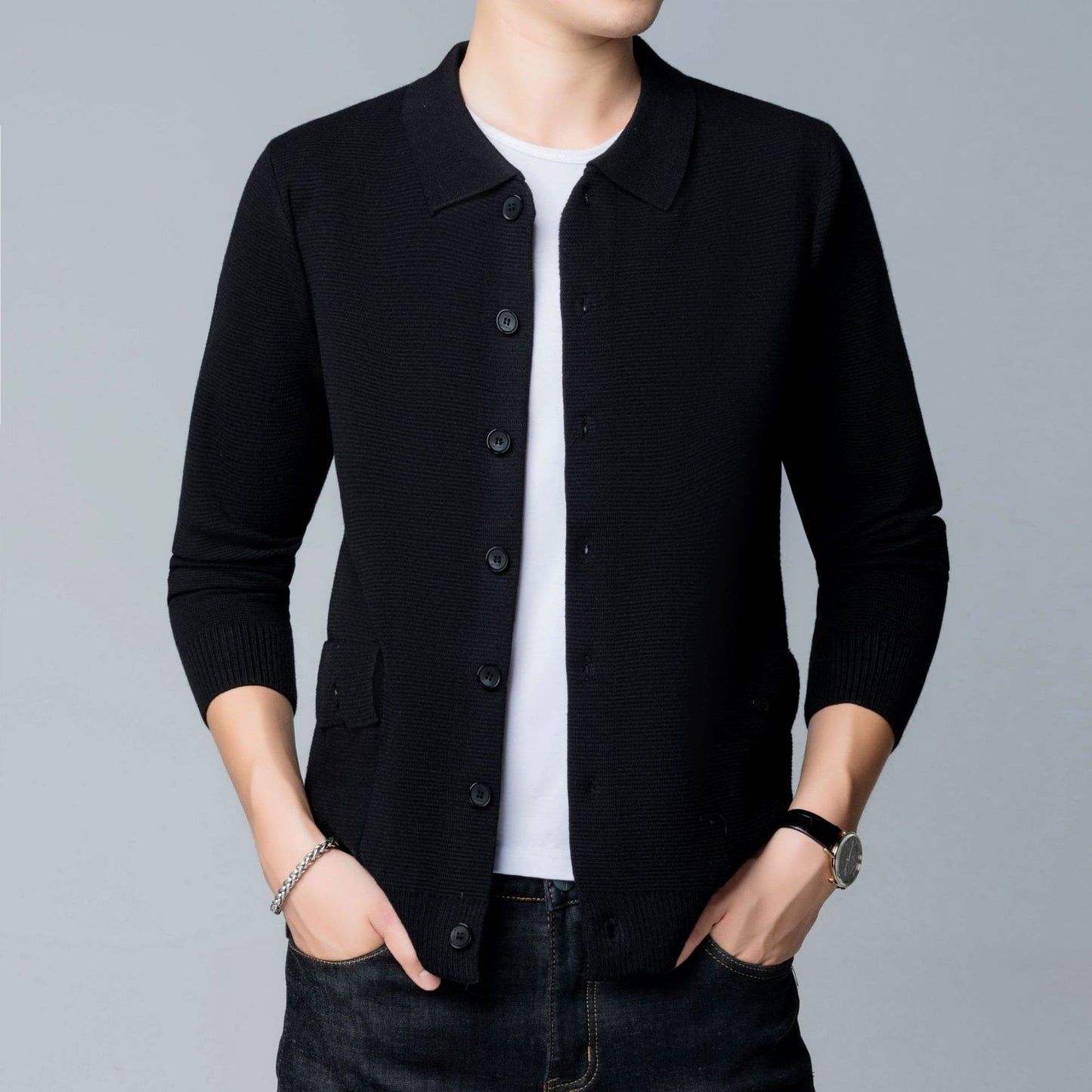 Mann in schwarzer Strickjacke, weißem T-Shirt und Jeans. Mode, Herrenbekleidung, lässiger Stil, Armbanduhr, grauer Hintergrund.