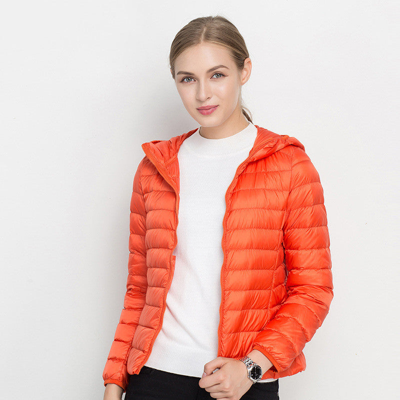 Frau in orangefarbener Daunenjacke, weißem Pullover, lächelnd, vor weißem Hintergrund. Modetrend, Winterjacke, Damenbekleidung.