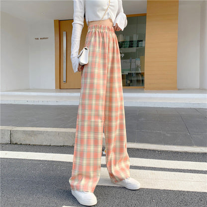 Frau in karierter, hoch taillierter Hose und weißem Langarmshirt, steht auf Gehweg. Modetrend, Streetstyle, lässige Damenmode.