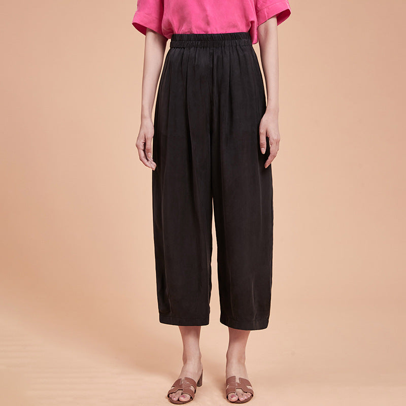 Frau in schwarzer, weiter Hose und pinkem T-Shirt vor beigem Hintergrund. Modetrend, lässiger Stil, Sommermode, Damenbekleidung.