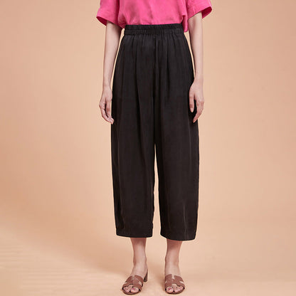 Frau in schwarzer, weiter Hose und pinkem T-Shirt vor beigem Hintergrund. Modetrend, lässiger Stil, Sommermode, Damenbekleidung.