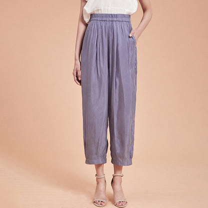 Frau in lila, hoch taillierter, weiter Hose aus Seide, kombiniert mit weißem Oberteil und Sandalen. Elegante Damenmode, Sommeroutfit.