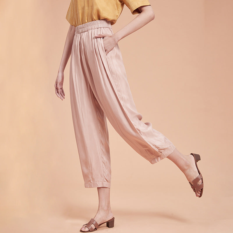 Frau in rosa Satin-Hose und gelbem Oberteil, trägt braune Sandalen. Modetrend, elegante Damenbekleidung, bequeme Sommerhose.