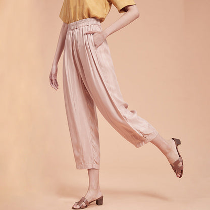 Frau in rosa Satin-Hose und gelbem Oberteil, trägt braune Sandalen. Modetrend, elegante Damenbekleidung, bequeme Sommerhose.