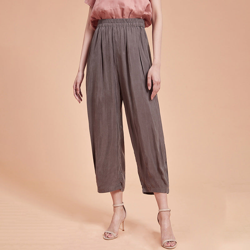 Frau trägt weite, graue Culotte-Hose und rosa Bluse, steht auf beigem Hintergrund. Modetrend, Damenbekleidung, elegante Sommermode.