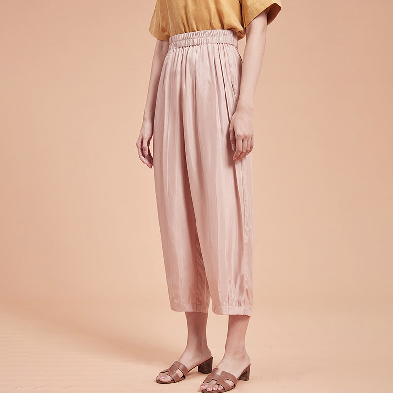 Frau trägt weite, rosa Seidenhose und gelbes Oberteil, stehend vor beigem Hintergrund. Modetrend, Damenbekleidung, elegante Sommerhose.