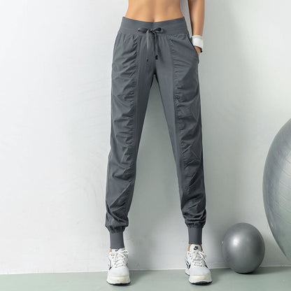 Frau in grauer Jogginghose und weißen Sneakers, stehend neben einem Gymnastikball. Sportbekleidung, Fitnessmode, bequeme Trainingshose.