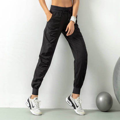 Frau in schwarzen Jogginghosen und weißen Sneakers steht neben einem Gymnastikball. Sportliche Kleidung, Fitnessmode, Freizeitlook.