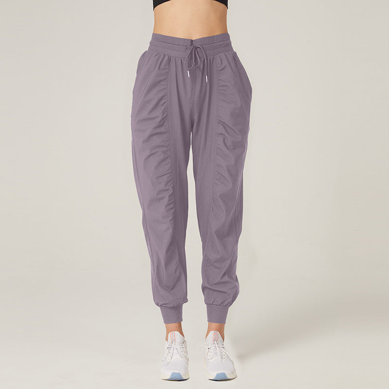 Frau in lila Jogginghose und weißen Sneakers vor neutralem Hintergrund. Bequeme Sportbekleidung, modische Damenhose, Freizeitlook.