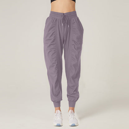 Frau in lila Jogginghose und weißen Sneakers vor neutralem Hintergrund. Bequeme Sportbekleidung, modische Damenhose, Freizeitlook.