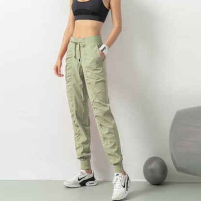 Frau in sportlicher Kleidung, trägt grüne Jogginghose und schwarzen Sport-BH, steht neben einem Gymnastikball. Fitnessmode, Sportbekleidung, Workout.