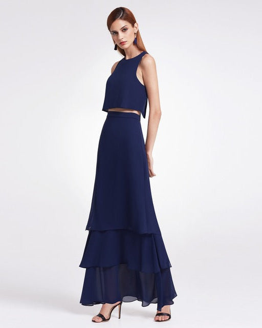 Frau in elegantem, dunkelblauem Abendkleid mit Stufenrock und ärmellosem Oberteil, trägt schwarze High Heels. Perfekt für formelle Anlässe.