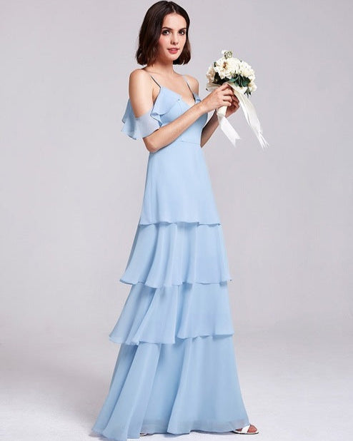 Frau in hellblauem, schulterfreiem Abendkleid mit Rüschen, hält Blumenstrauß. Elegantes, modernes Design, ideal für Hochzeiten oder formelle Anlässe.