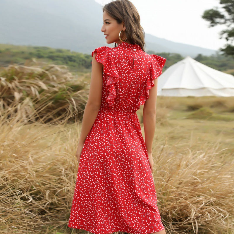 Frau im roten, gepunkteten Sommerkleid mit Rüschen steht in einer natürlichen Landschaft. Hintergrund zeigt Zelt und Hügel. Outdoor-Mode, Sommerkleid.