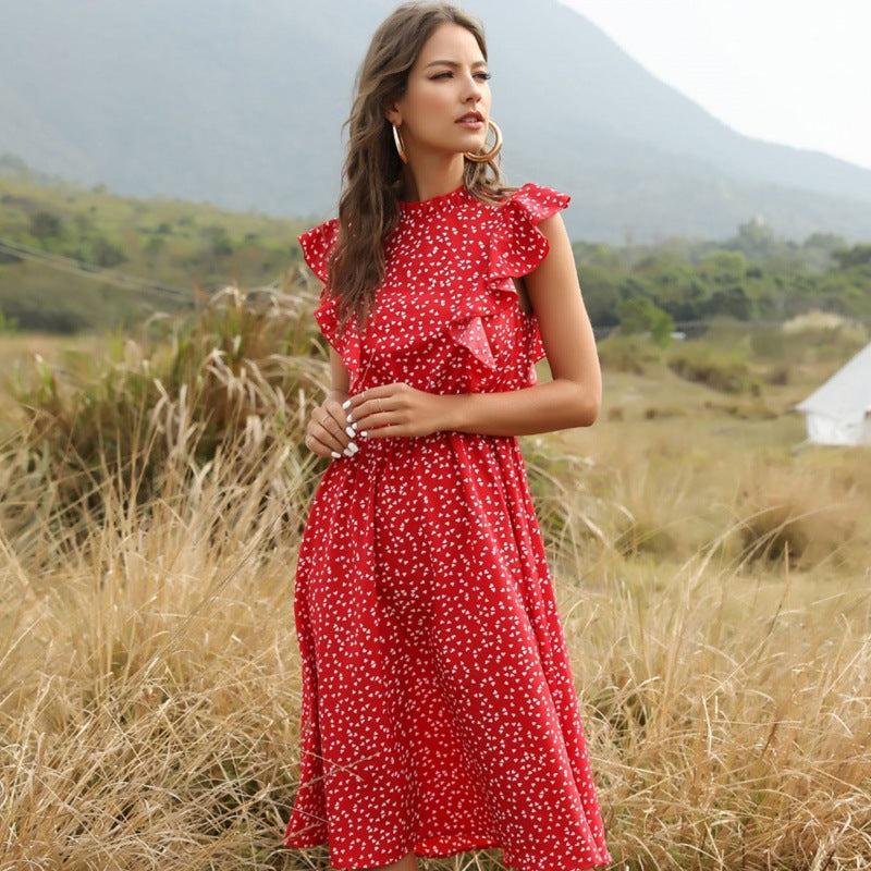 Frau in rotem, gepunktetem Kleid steht auf einer Wiese vor Berglandschaft. Sommermode, Freizeitkleidung, Naturhintergrund.