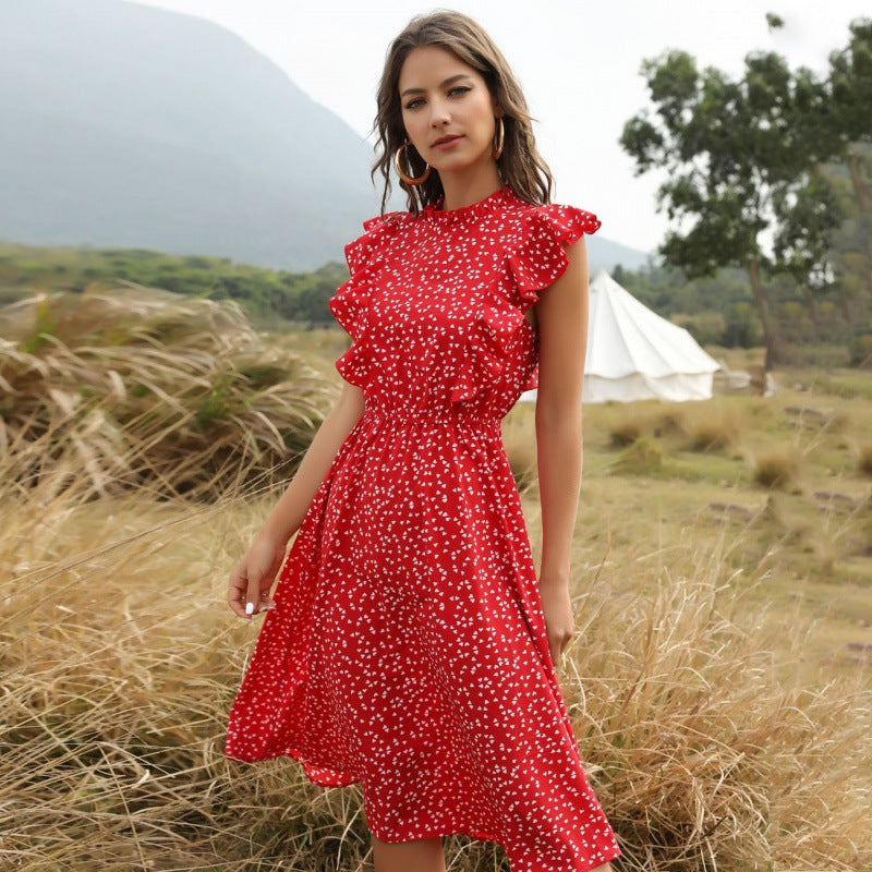 Frau in rotem, gepunktetem Kleid mit Rüschen steht auf einer Wiese vor einem Zelt. Sommermode, Outdoor, stilvolles Kleid, Naturhintergrund.